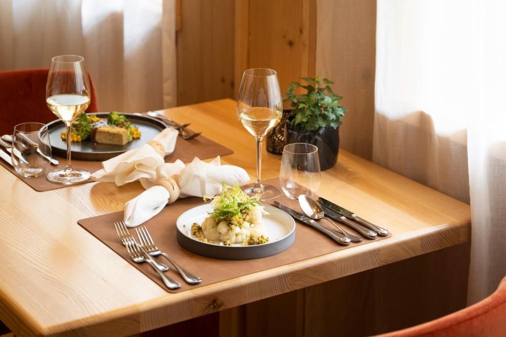 A dining table set with plates, cutlery, and glasses of white wine.