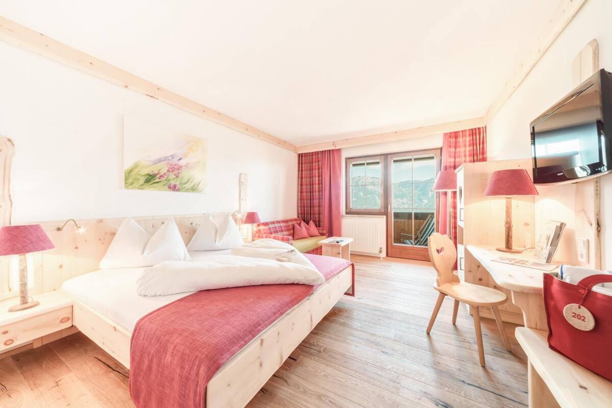 Une chambre d’hôtel avec un lit, un bureau, une chaise, une télévision et une fenêtre avec des rideaux.