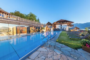 A pool area with a stone pathway, lounge chairs, and wooden buildings with balconies. - Natur & Wellnesshotel Höflehner (Haus)