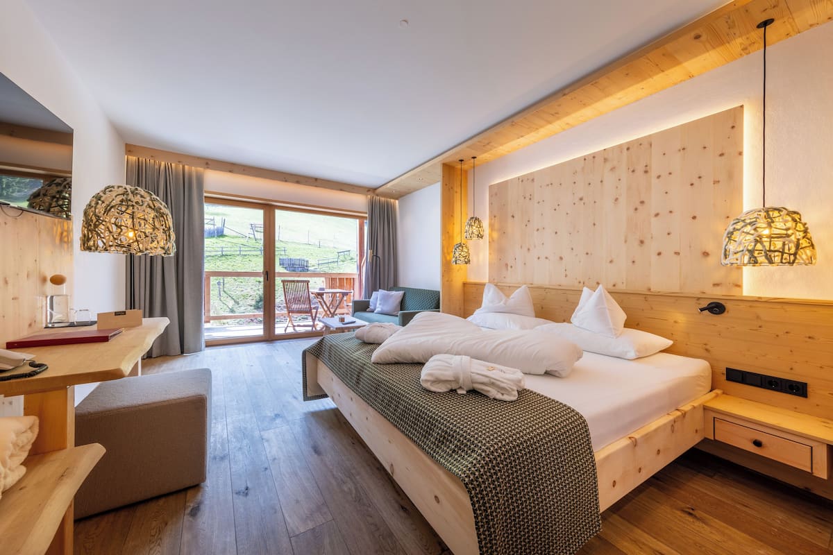 Une chambre d’hôtel moderne avec un lit en bois, un bureau et un balcon offrant une vue sur la campagne.