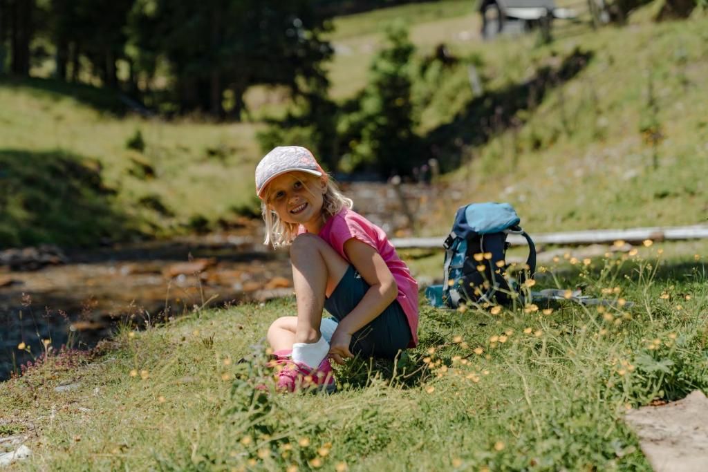 Eine Person sitzt mit Rucksack im Gras in der Nähe eines Baches.
