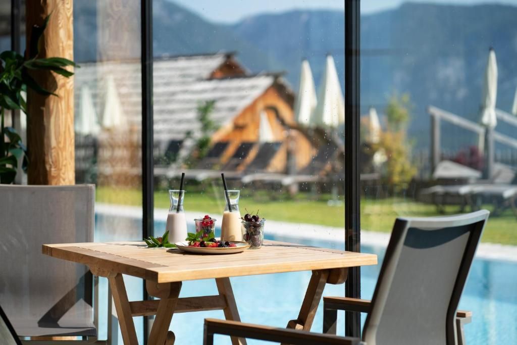 A wooden table with a glass of milk, a glass of water, and a plate of food, with a view of a pool and mountains in the background.