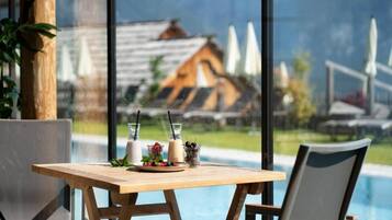 A wooden table with a glass of milk, a glass of water, and a plate of food, with a view of a pool and mountains in the background.