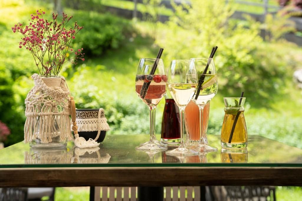 Una mesa de vidrio con cuatro bebidas y un florero de macramé con flores.