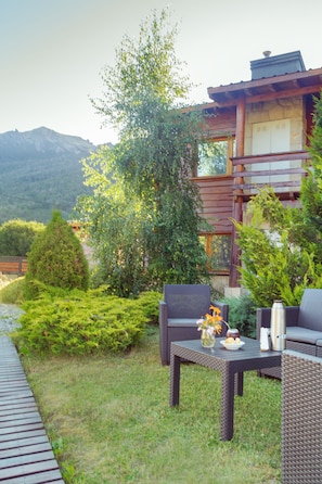 An outdoor seating area with wicker furniture, a table with a vase and a bowl, and a view of mountains in the background.