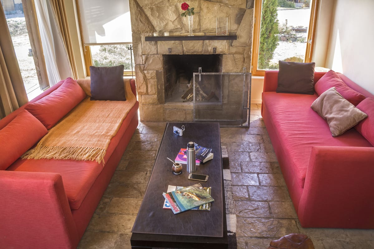 A cozy living room with a stone fireplace, red sofas, and a coffee table with books and a camera.
