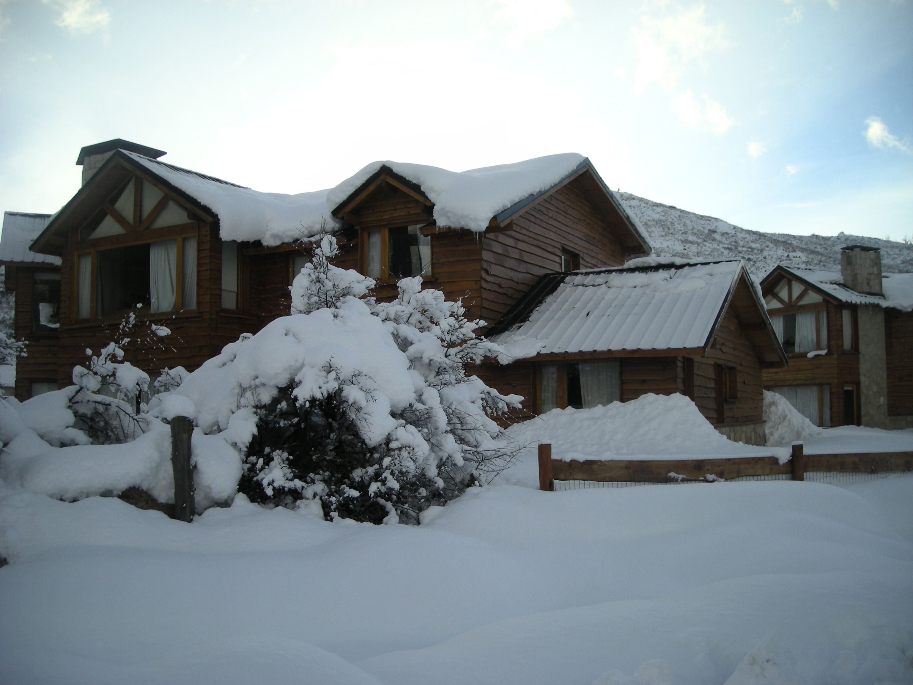 A wooden cabin with a snow-covered roof and a wooden fence in front.