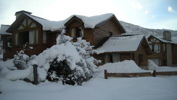 A wooden cabin with a snow-covered roof and a wooden fence in front.