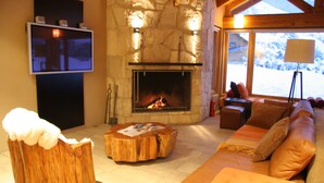 A cozy living room with a stone fireplace, a television mounted on the wall, and a large window offering a view of the outdoors. - Galileo Boutique Hotel (San Carlos de Bariloche)