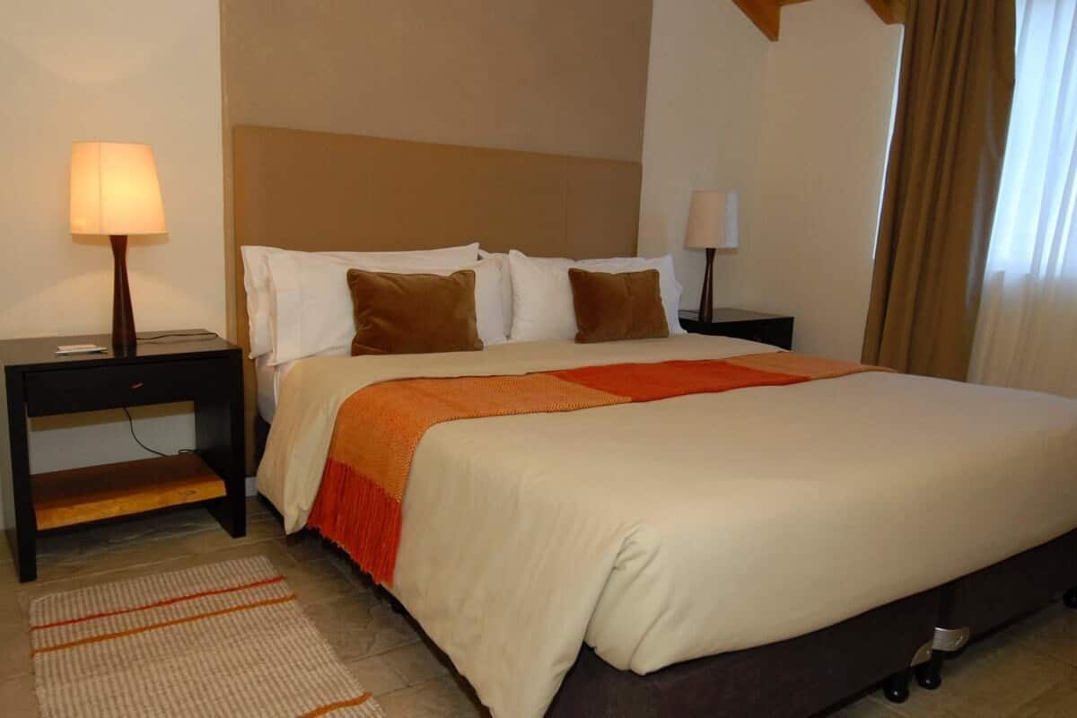 A hotel room with a bed, two bedside tables, a lamp on each table, a rug, and a window with curtains.