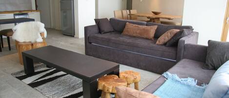 A modern living room with a sofa, coffee table, and a dining area with a table and chairs.
