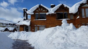 Eine Holzhütte mit schneebedeckten Dächern und Fenstern, umgeben von einem Schneehaufen.
