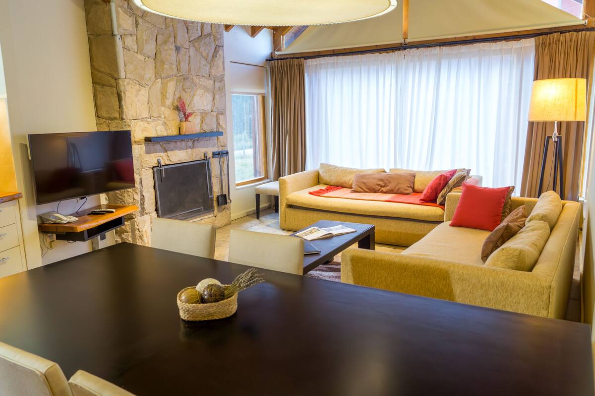 A furnished living area with a stone wall, a flat-screen TV, a sofa, a coffee table, and a dining table.