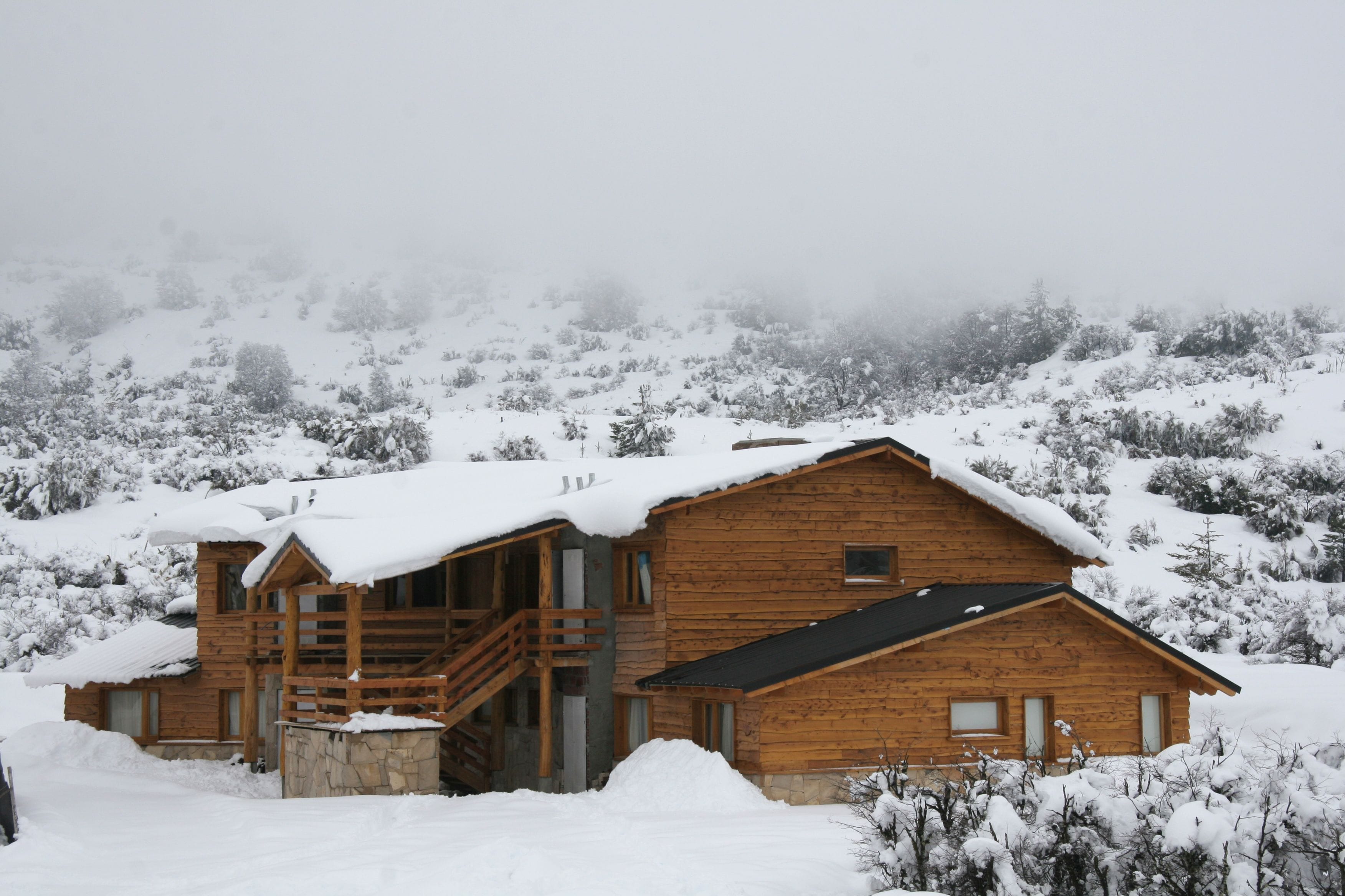 A wooden cabin with a staircase leading to the entrance, surrounded by snow-covered trees.
