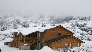 A wooden cabin with a staircase leading to the entrance, surrounded by snow-covered trees.