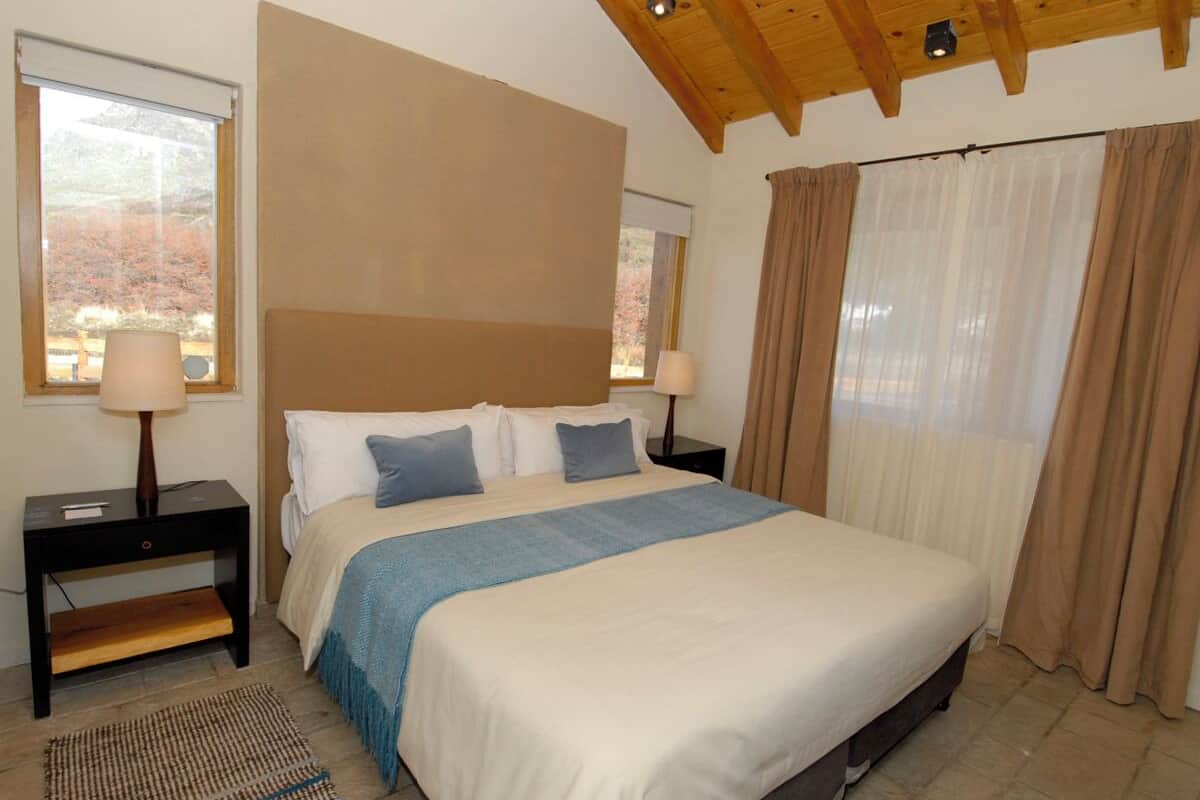 A bedroom with a large bed, two bedside tables with lamps, a window with a view, and a ceiling with wooden beams.