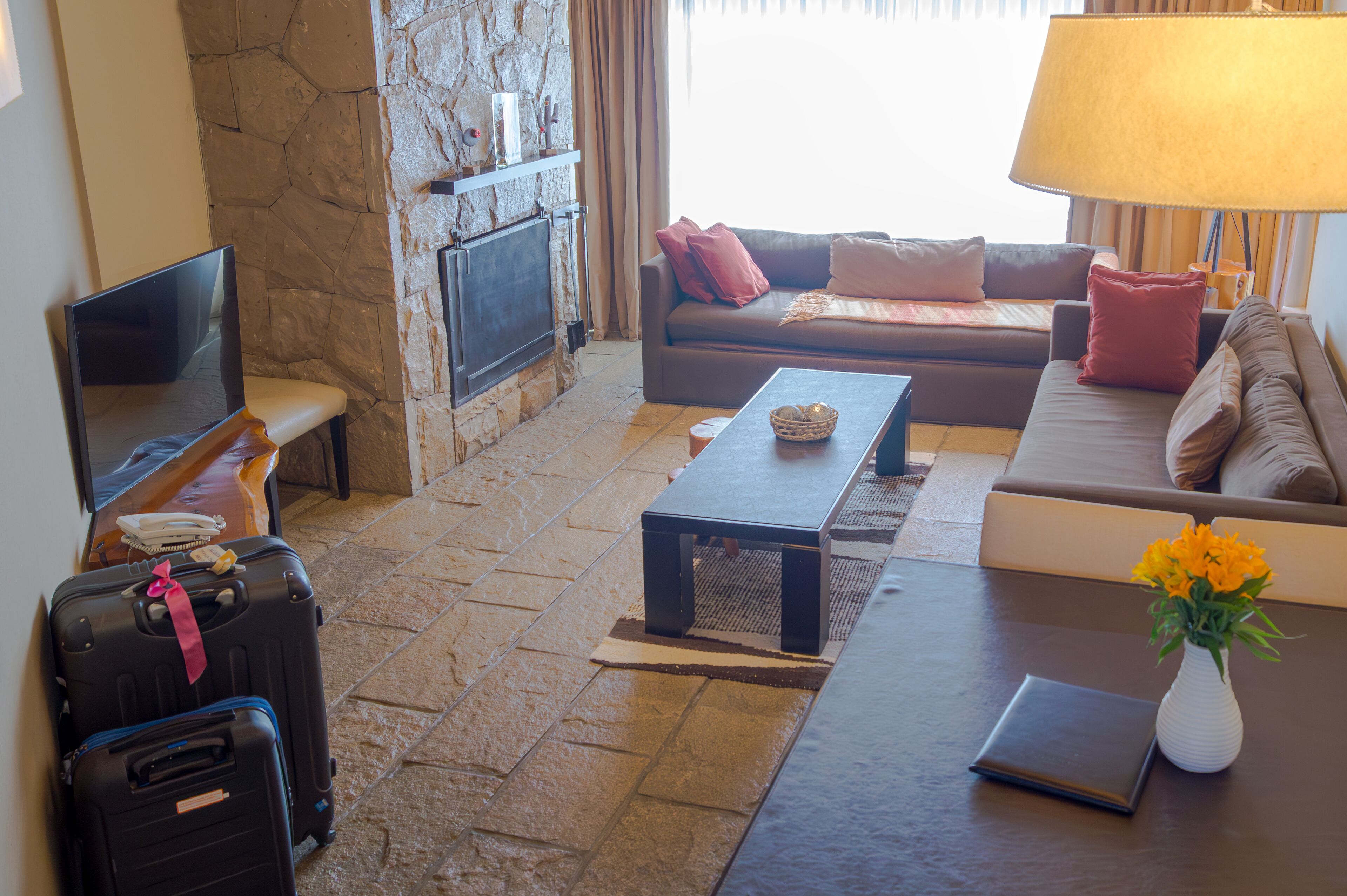 Una sala de estar con chimenea de piedra, un sofá, una mesa de centro, un televisor y equipaje.