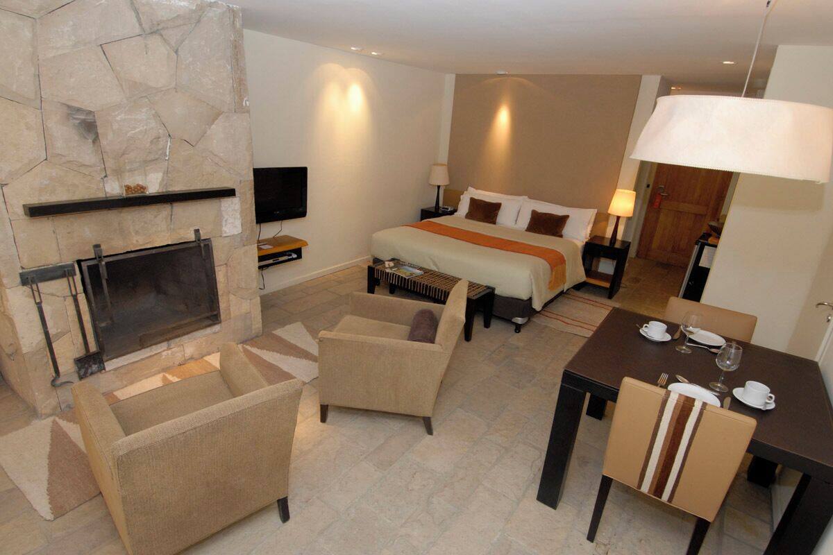 A hotel room with a fireplace, a bed, a TV, a dining table with chairs, and a lamp.