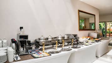 Montaje de bufé con distintas estaciones de comida, una máquina de café y un espejo grande en la pared.