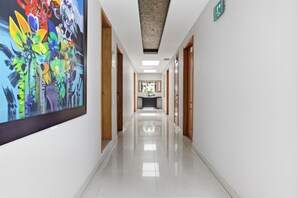 Een hotelgang met een groot abstract schilderij aan de linkerkant, houten deuren aan beide zijden en een groen vluchtroutebord aan de rechterkant.