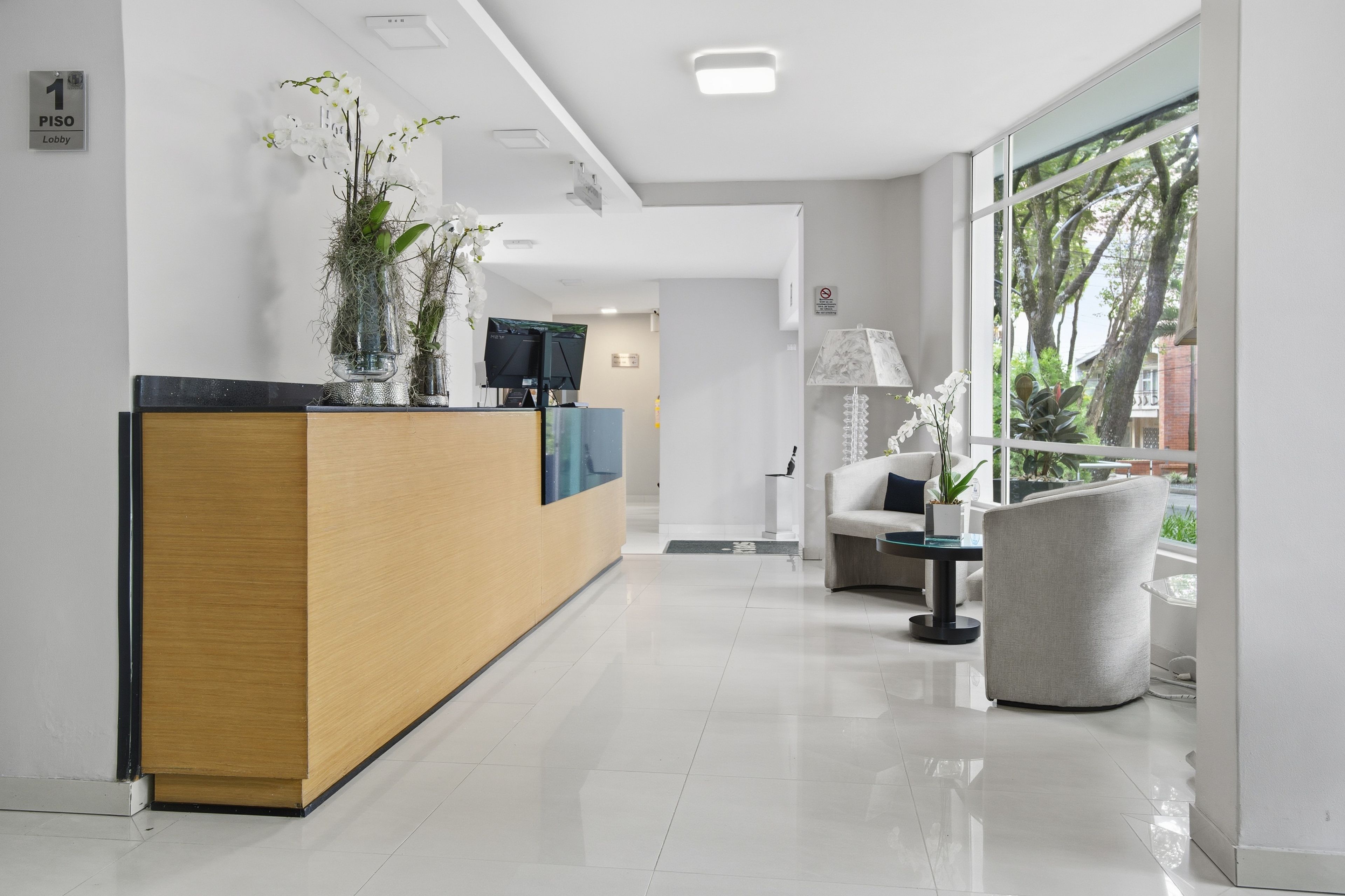 Un espace d’accueil moderne comprenant un comptoir de réception en bois, un téléviseur à écran plat et un coin salon avec un canapé et un fauteuil.