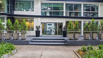 Une entrée d’hôtel moderne avec une façade en verre, des sièges en plein air et des plantes en pot.