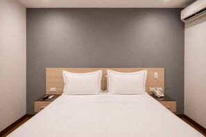 A hotel room with a large bed, two bedside tables, a wall-mounted air conditioner, and a wooden headboard. - Hotel Asturias Medellin (Medellín)
