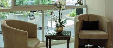 Una habitación con dos sillones, una pequeña mesa con una planta y ventanas amplias que dan a vista de árboles y edificios.