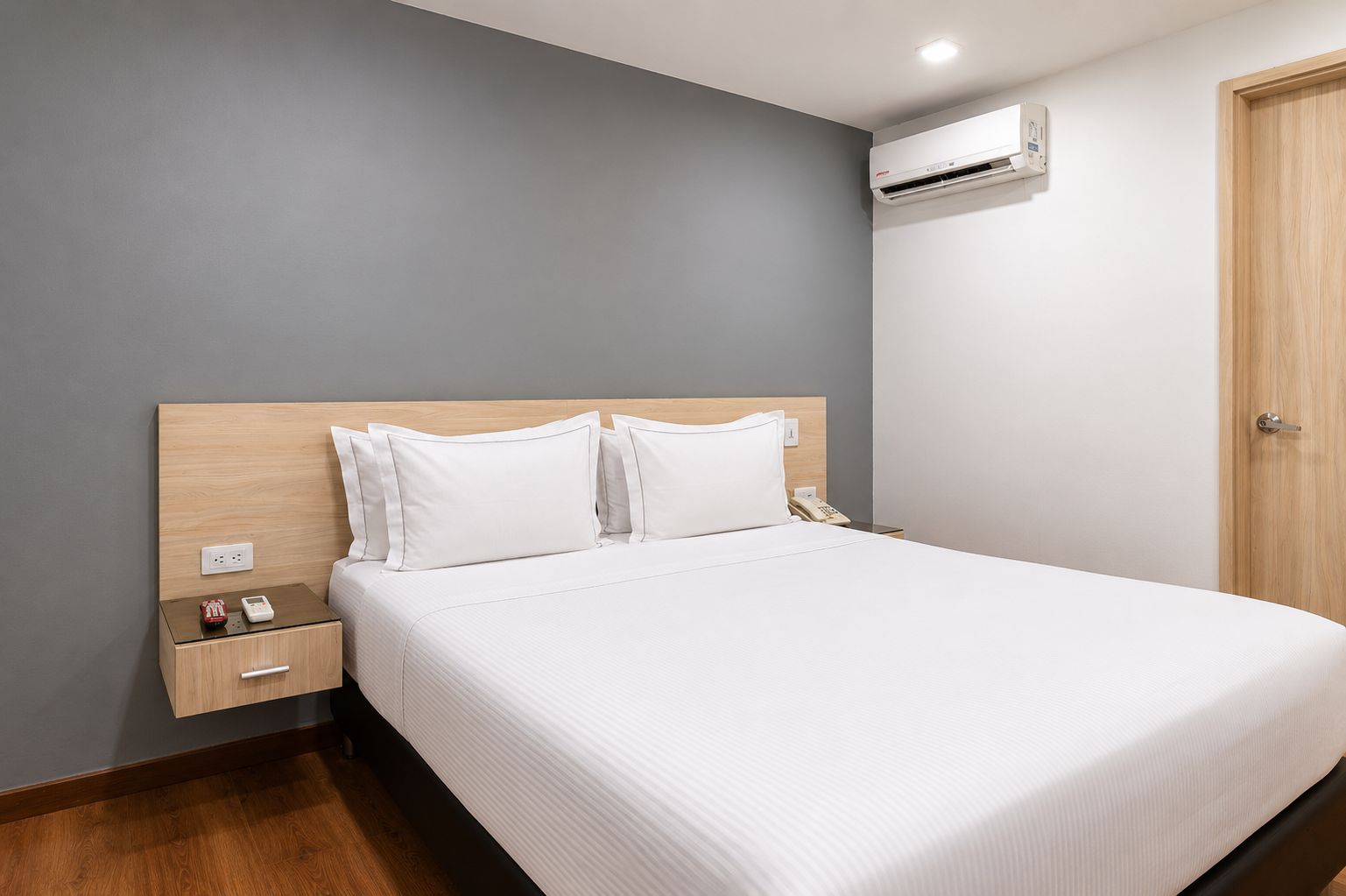 Una habitación de hotel con cama, mesita de noche y aire acondicionado.