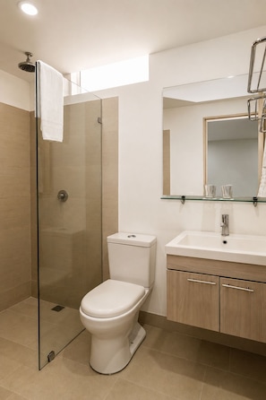 A modern bathroom with a glass-enclosed shower, a toilet, a sink with a mirror, and wooden cabinets. - Hotel Asturias Medellin (Medellín)