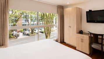 A hotel room with a large bed, a TV, a desk, and a view of the street.