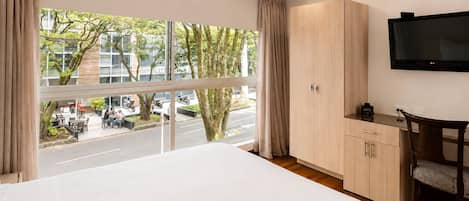 Habitación de hotel con una cama grande, televisión, escritorio y vista a la calle.