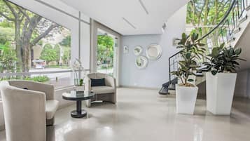 Un vestíbulo moderno con un sofá, sillas, una mesa de vidrio, plantas en macetas y una escalera.
