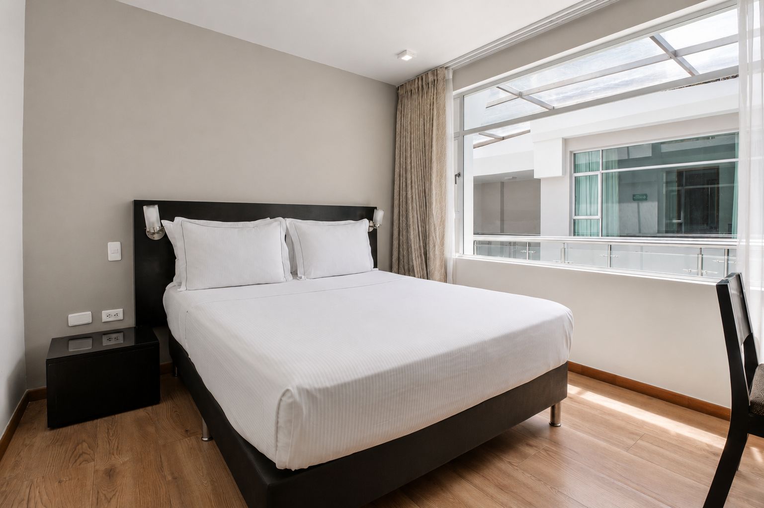 Habitación de hotel con cama, mesita de noche, ventana con vistas y una silla.