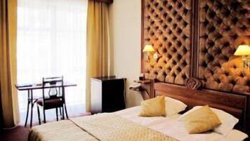 A hotel room with a large bed, a wooden headboard, a desk, and a chair.