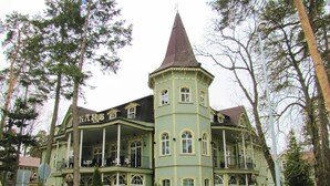 Ein großes, historisches Gebäude mit einem Turm, zahlreichen Fenstern und einer Veranda mit Außenbestuhlung.
