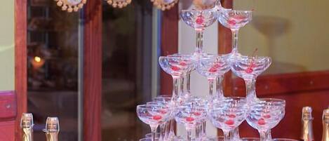 A table with a tiered glass display of red drinks, bottles of red wine, and a variety of appetizers.