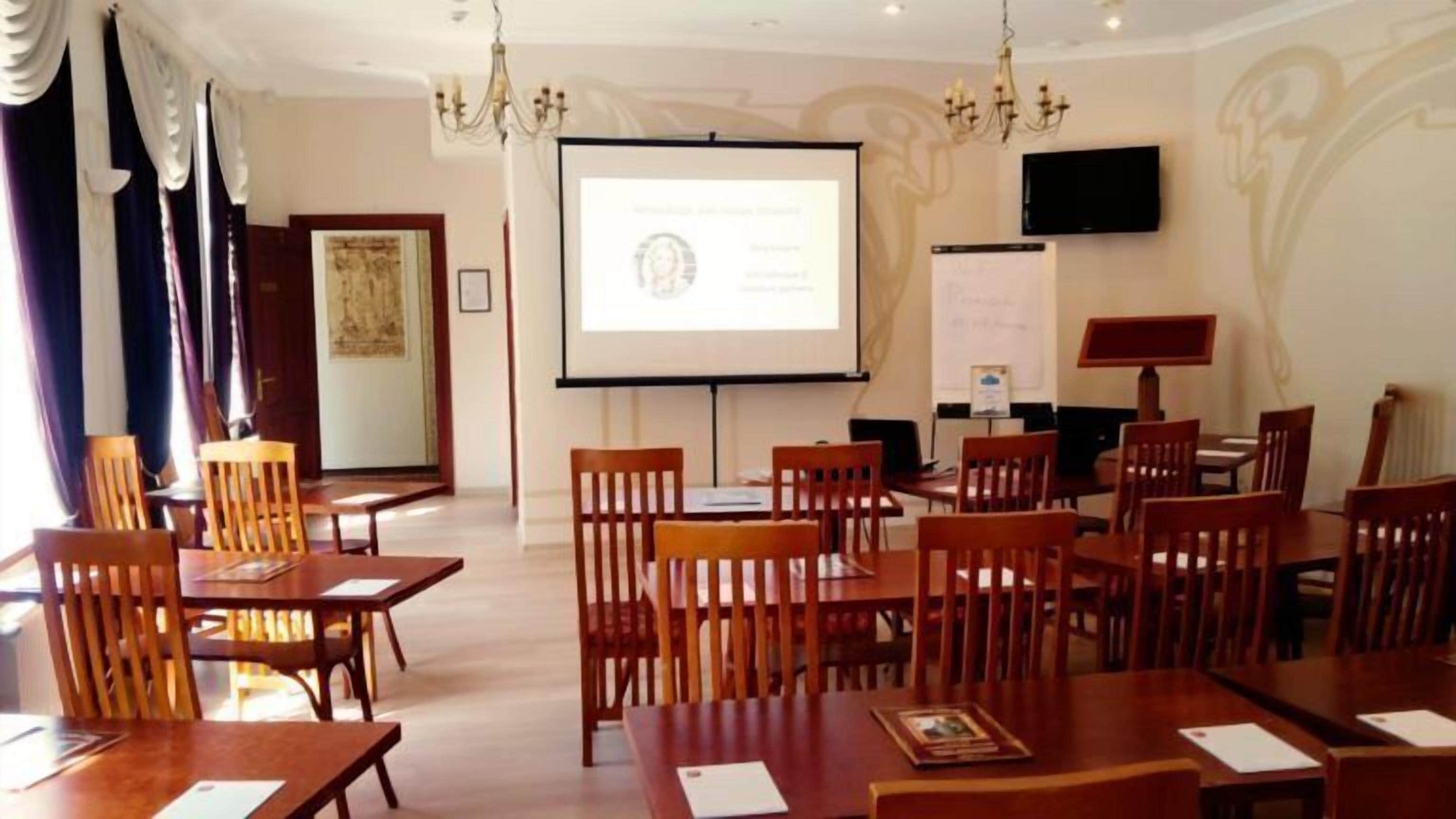 Un salón de conferencias con mesas y sillas de madera, una pantalla de proyector y una pizarra.