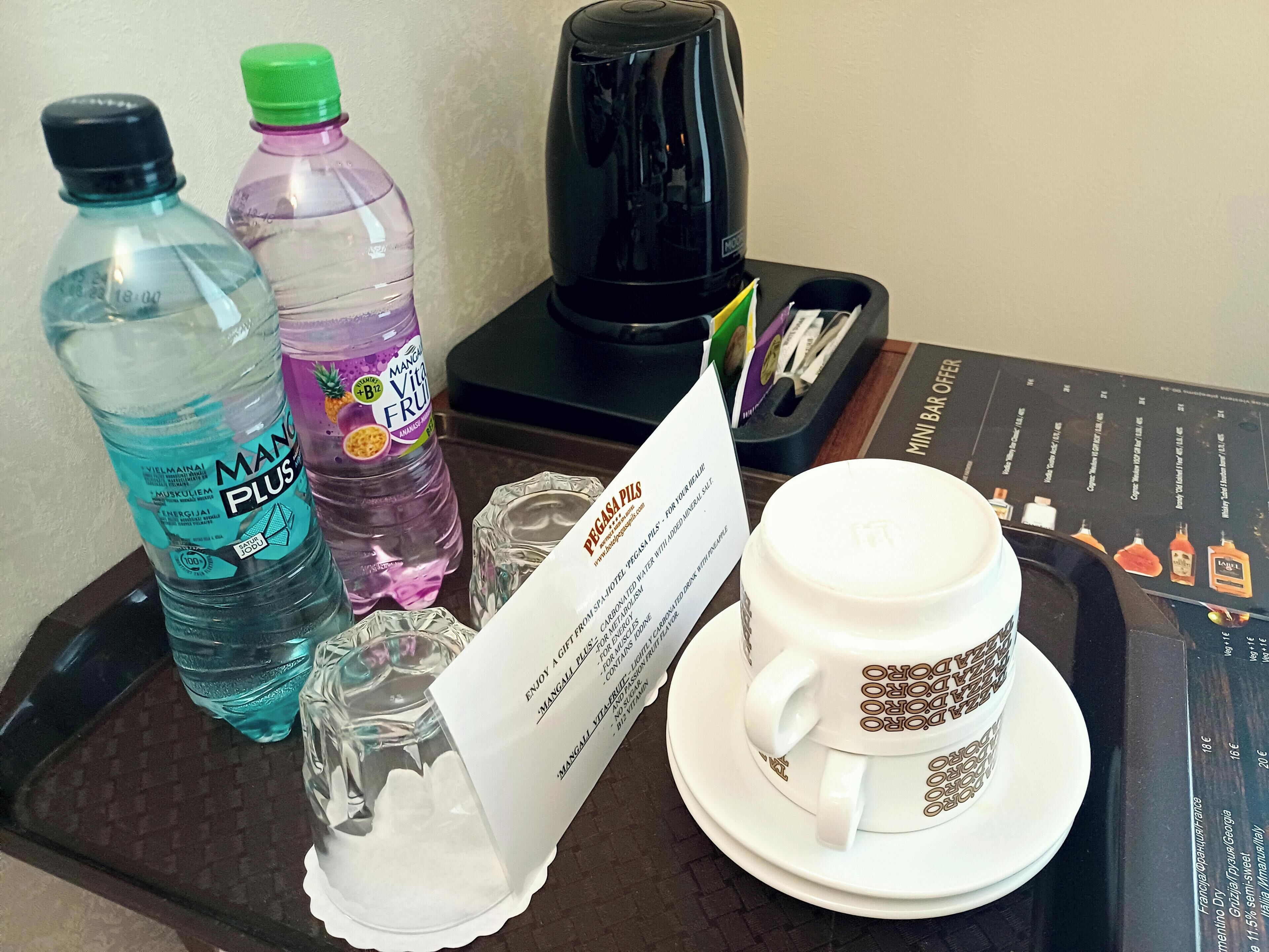 A tray with a coffee maker, two water bottles, a glass, and a cup with a saucer.