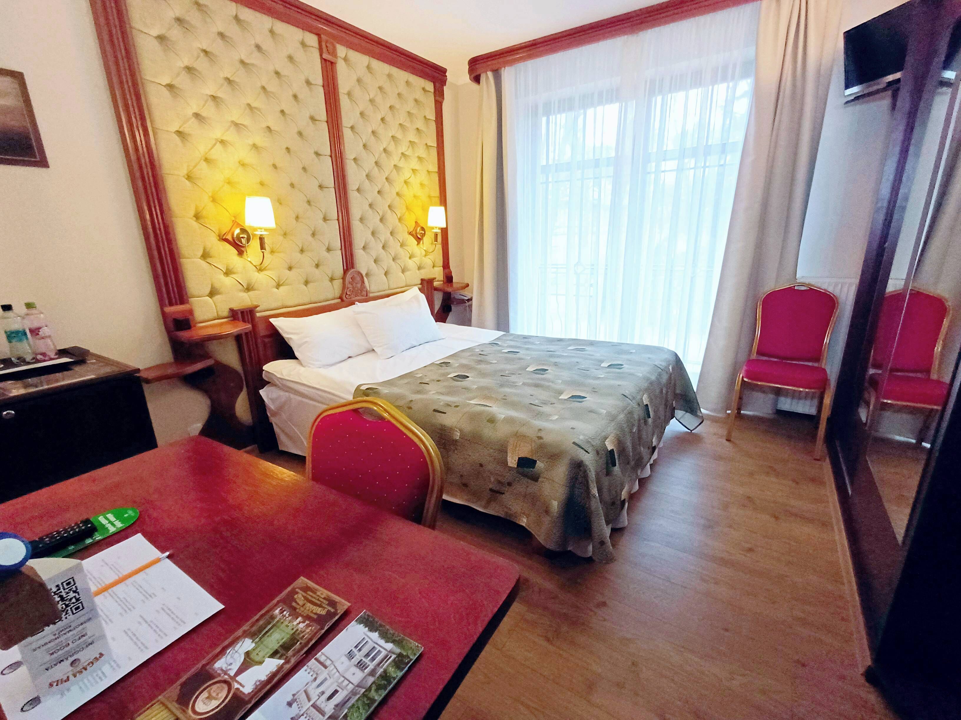 A hotel room with a large bed, two bedside lamps, a red armchair, a desk with a chair, and a TV mounted on the wall.
