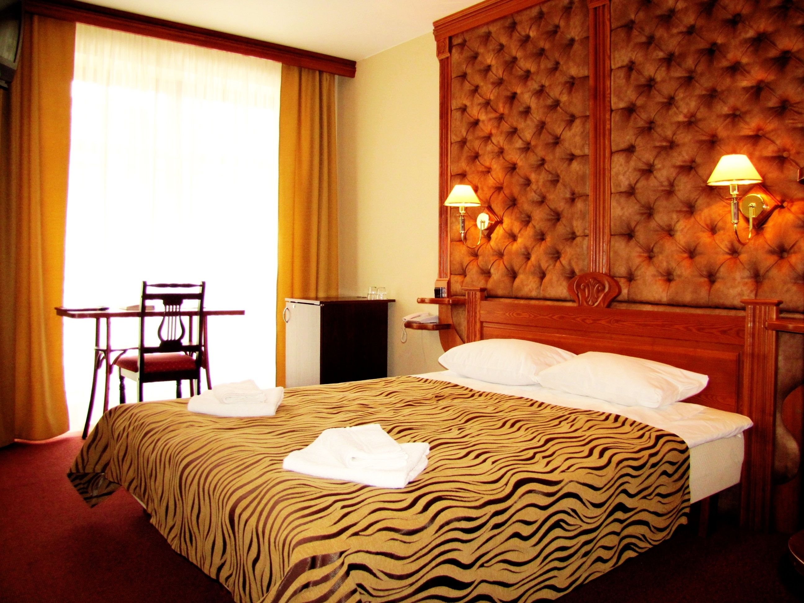 Une chambre d’hôtel avec un grand lit, une tête de lit en bois, deux lampes de chevet, un bureau avec une chaise et une fenêtre avec des rideaux.