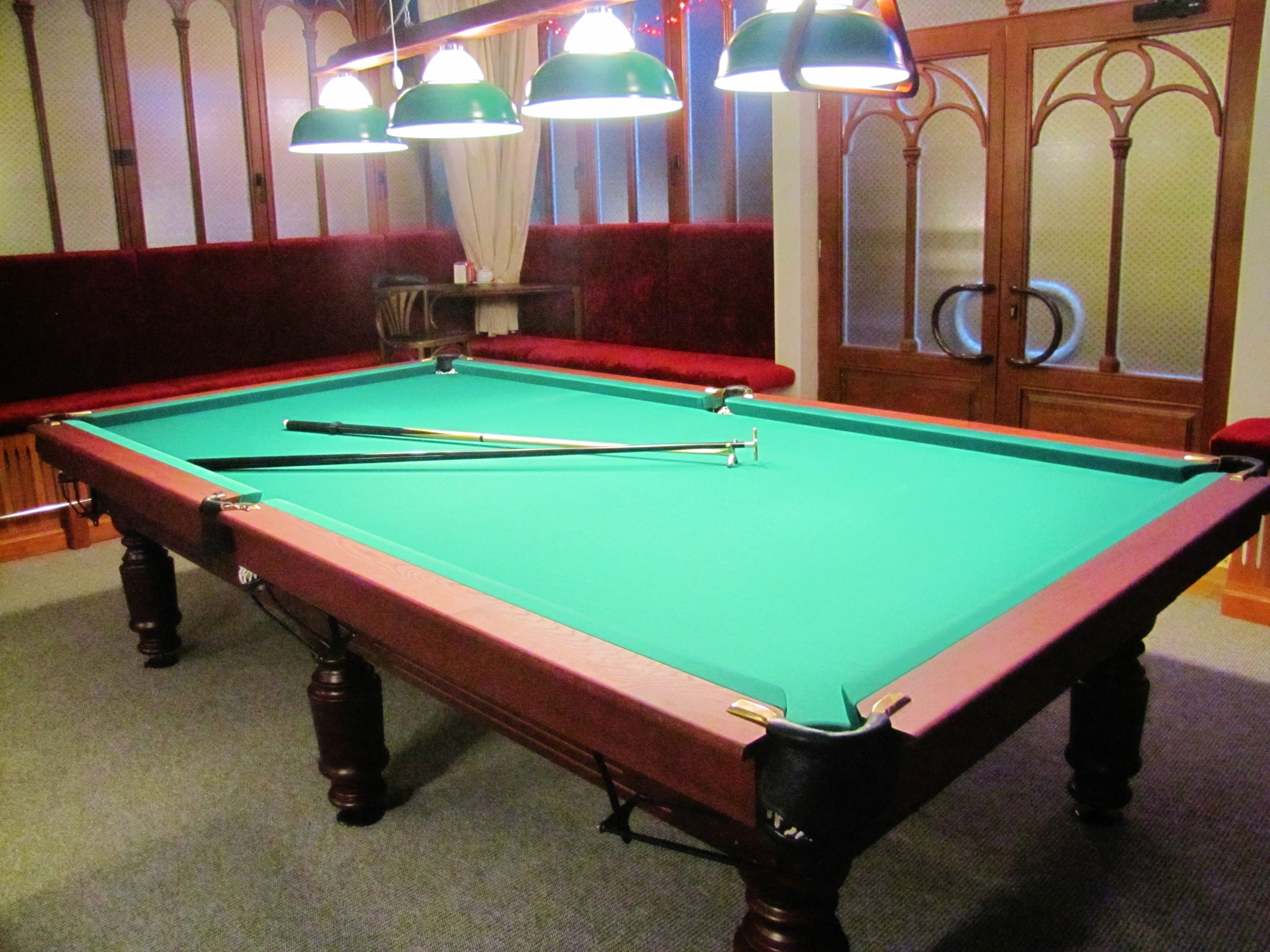 A pool table with three overhead lamps, a red cushioned bench, and a wooden cabinet with glass doors.