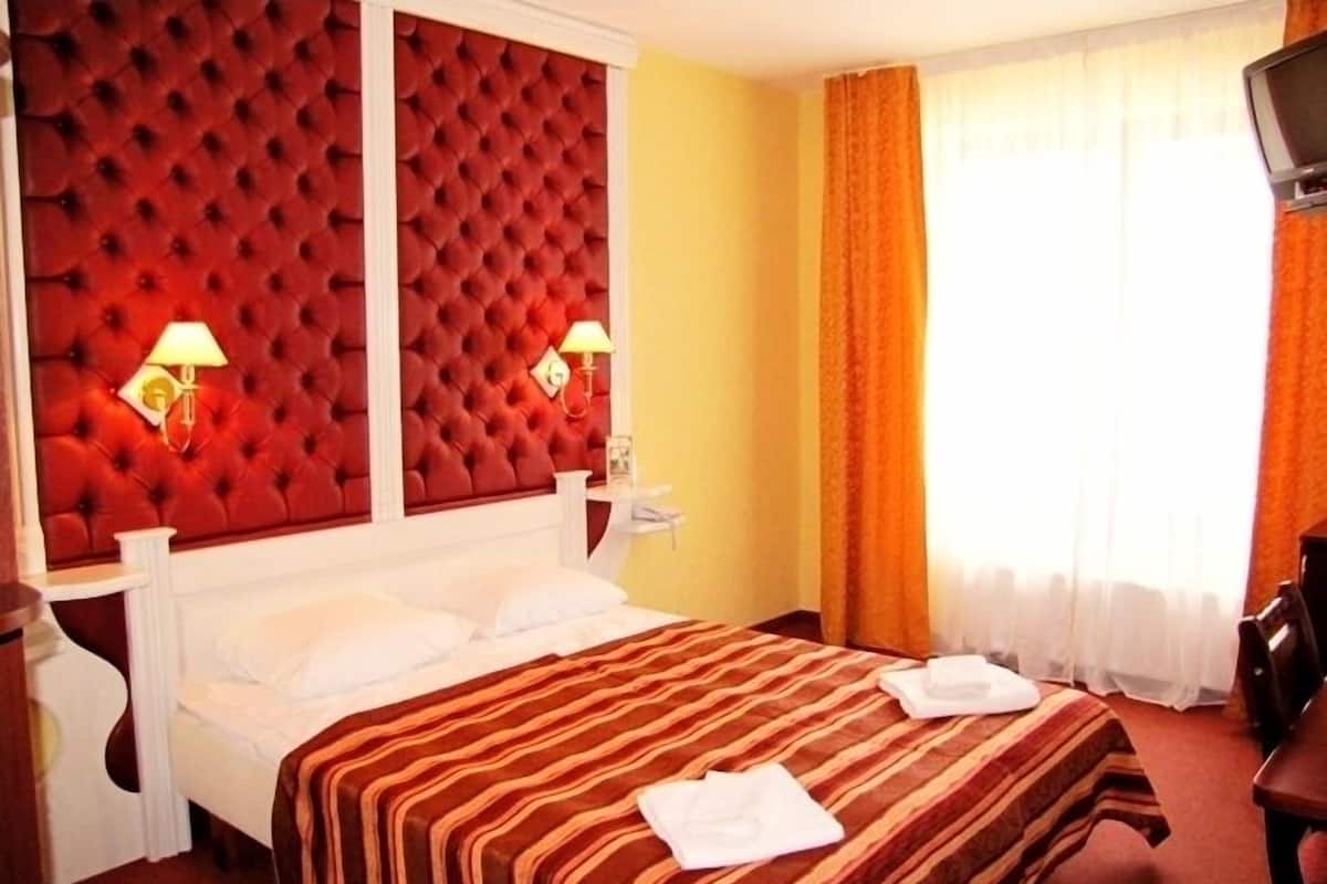 Et hotelværelse med en rødbed fremhævet sengegavl, et stribet sengetæppe og et fjernsyn på et træstel.