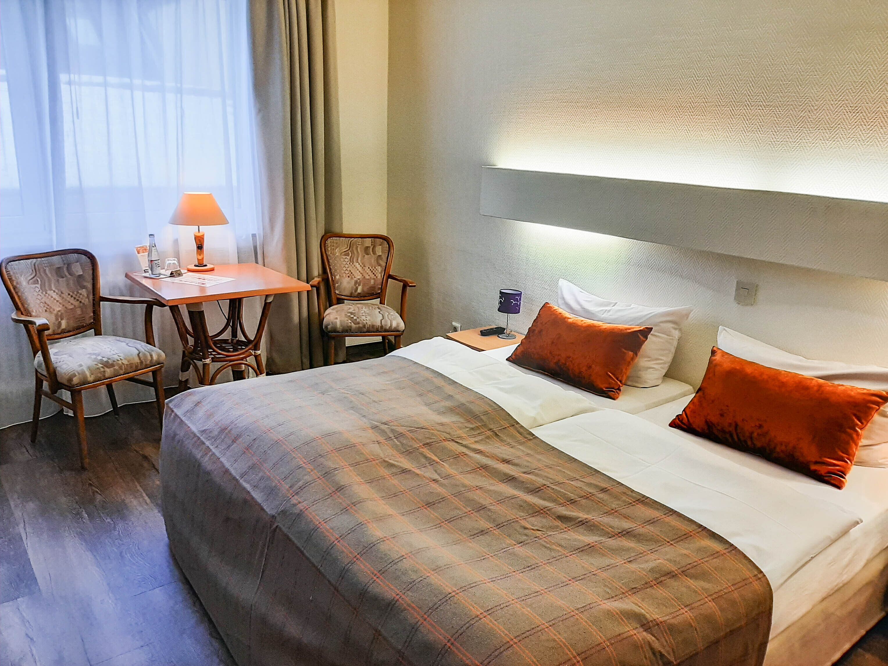 A hotel room with a large bed, two chairs, a small table, and a lamp.