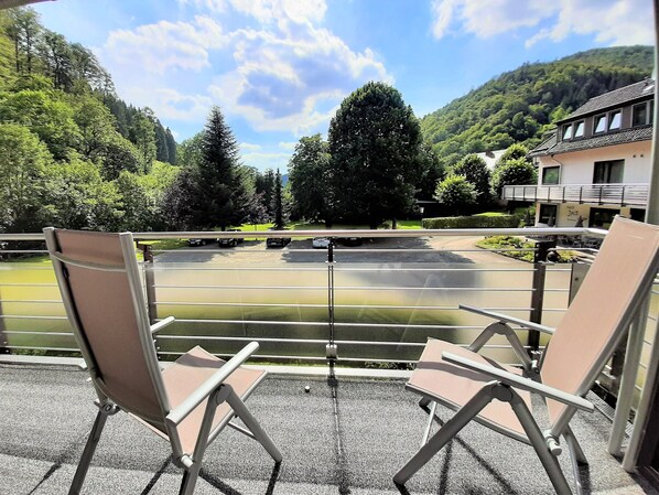 A terrace with two lounge chairs, a view of a lake, and a building in the background.