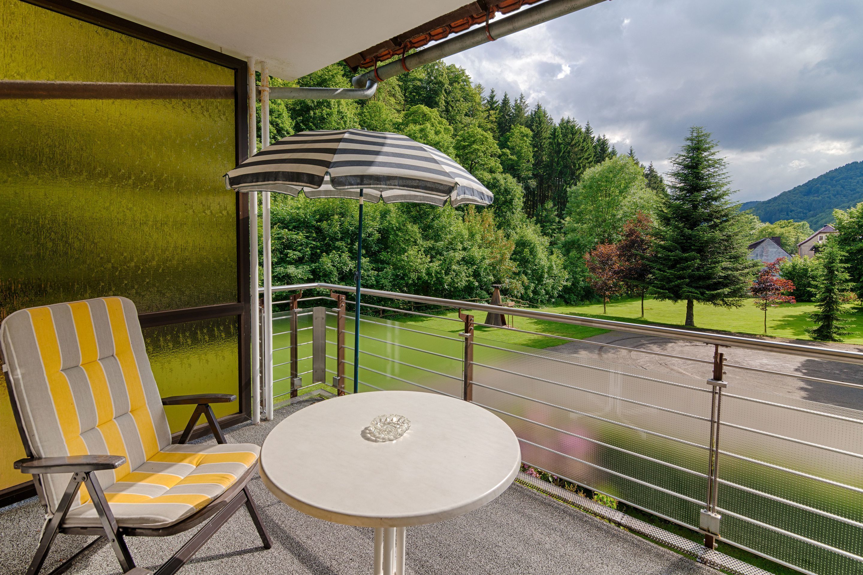 Un balcone con una sedia e un tavolino, entrambi decorati con strisce, e un ombrellone a righe.