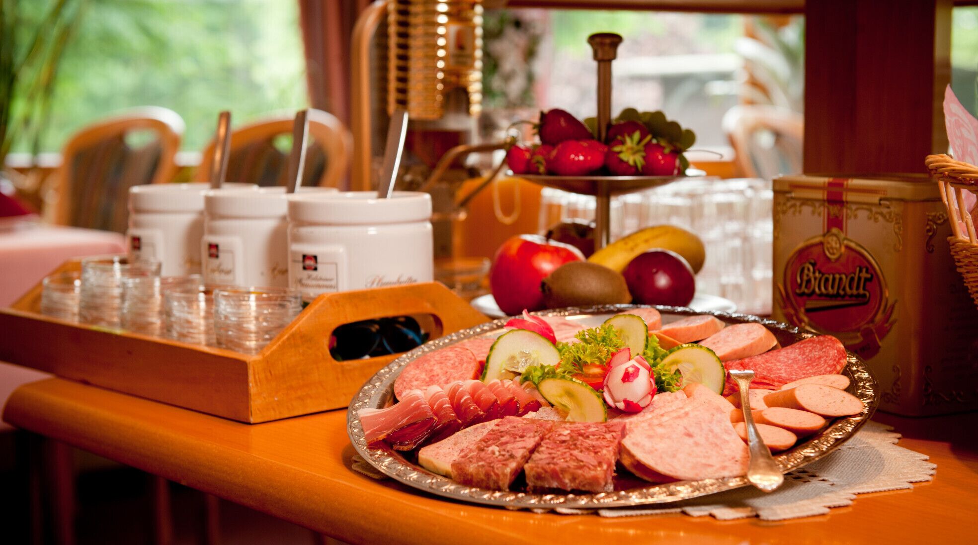 Une table garnie d’une variété d’aliments, notamment des charcuteries, des fruits et une bouteille de spiritueux.