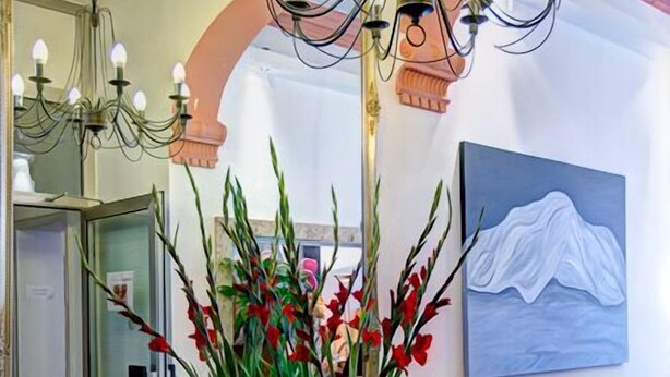 Uma sala de jantar com um candelabro, cadeiras, uma mesa com frutas e um quadro na parede.