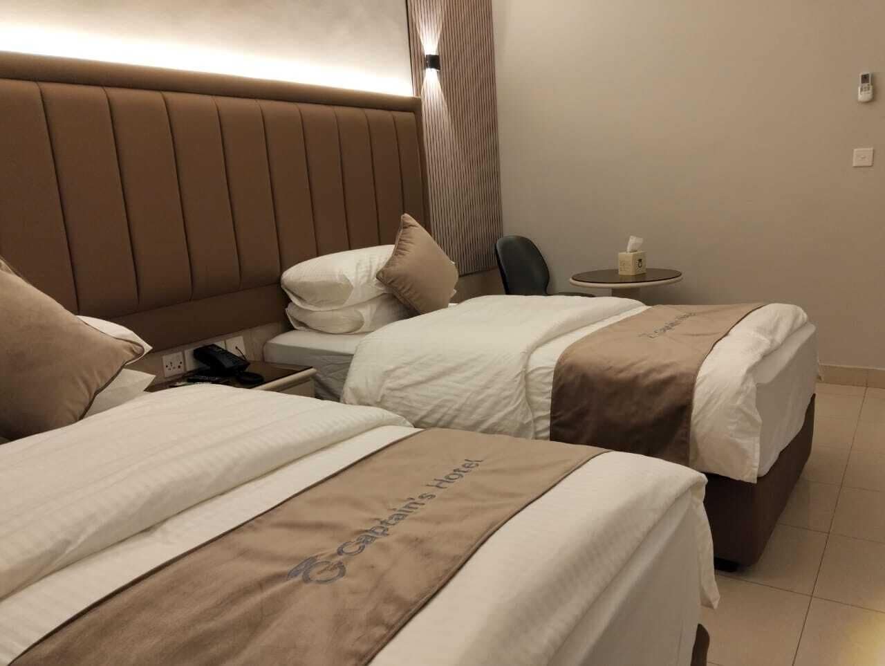 A hotel room with two beds, a bedside table with a lamp, and a small table with a tissue box.