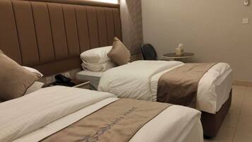 A hotel room with two beds, a bedside table with a lamp, and a small table with a tissue box.